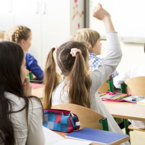 Little girl raising her hand to answer the teacher's question in primary school